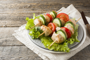 Traditional chicken kebab on wooden skewers with tomatoes, cucumbers and fresh herbs on a plate