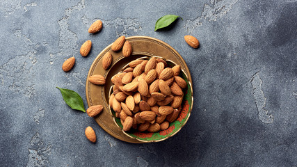 Almond nuts in bowl on gray concrete background with copy space. Top view.