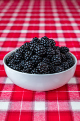 Vertical bowl of fresh picked blackberries, white ceramic bowl, red and white plaid tablecloth