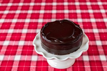 Round chocolate cake on a white ceramic cake plate, red and white plaid tablecloth