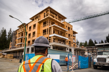 Construction worker in a hardhat observes an apartment complex under construction.