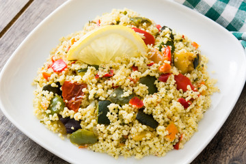 Couscous with vegetables in plate on wooden table