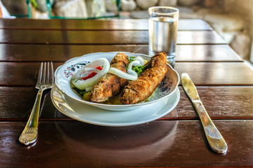Portion of a lamb kebab on a plate. Meat dish on a wooden brown table.