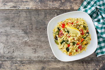 Couscous with vegetables in plate on wooden table. Top view. Copyspace
