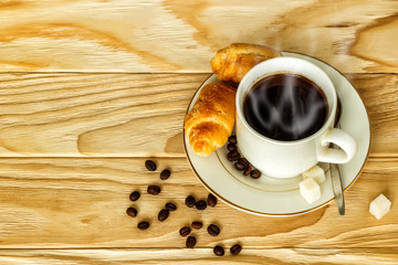 White cup with coffee and croissants on a wooden background, selective focus. The concept of breakfast.