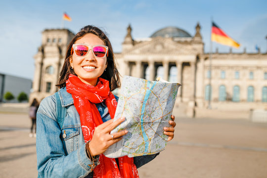 Beautiful young woman looking at map guide while standing in front of Bundestag building at sunset in Berlin. Travel in Germany concept