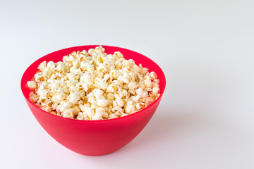 Popped popcorn in a big red plastic bowl on a white table