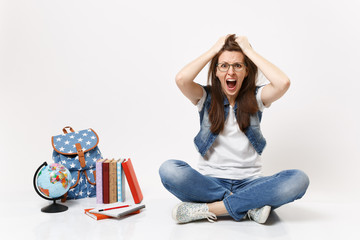 Young crazy dizzy woman student in denim clothes screaming clinging to head sitting near globe,...