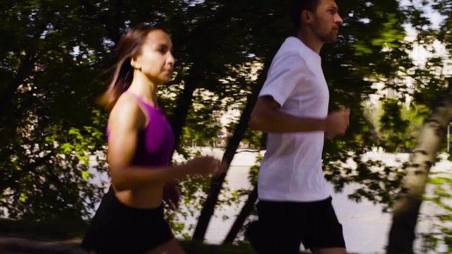 Dolly shot of young woman and man running in the city near the river. Side view