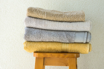Stack of clean folded terry towels on wooden high stool white wall background. Laundry spa wellness...
