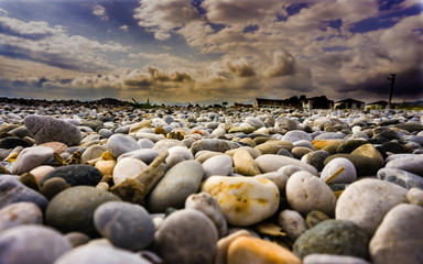Pile of colorful sea pebble stones and rocks on beach / coast. Different forms multicolor pebbles as natural abstract texture background. Close up colourful Distance background dramatic sky wallpaper.
