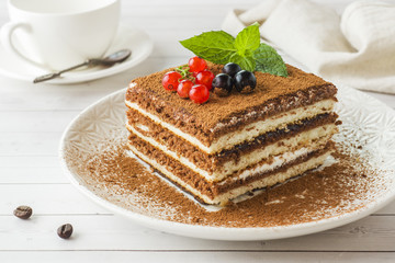 Delicious Tiramisu cake with fresh berries and mint on a plate on a light background. Breakfast with a Cup of coffee.