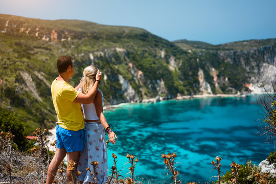 Birthday gift. Young man closing hes girlfriend eyes in front of gorgeous seascape panorama of blue lagoon. Couple love. Turquoise Petani beach on Kefalonia island Greece