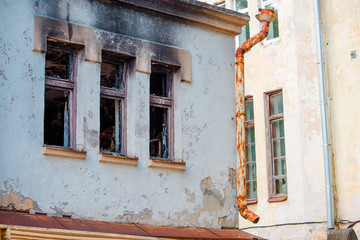 The facade of a burnt building with a rusty drainpipe and peeling walls
