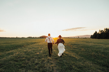 Wedding couple running in sunset lights on green field. Hipster wedding couple