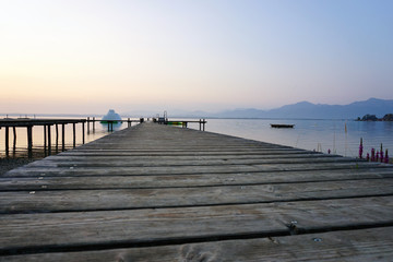 Naklejka premium bootssteg am chiemsee im sonnenaufgang mit alpen im hintergrund