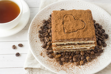 Delicious Tiramisu cake with coffee beans on a plate and a Cup of coffee on a light background