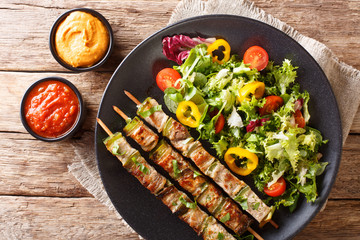 Delicious kebab on skewers with fresh vegetable salad on a plate and sauce close-up. horizontal top view