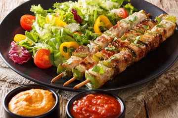 Grill kebab with vegetables on skewers with fresh salad on a plate and sauces close-up on a table. horizontal