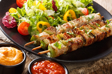 Spicy pork shish kebab with green pepper on skewers with fresh salad on a plate and sauces close-up. horizonta