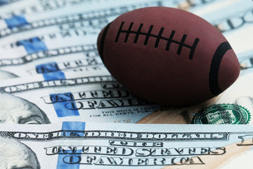 The concept of corruption or sports betting. Close-up of a symbol of rugby or American football on a background of hundred dollar bills in the USA.