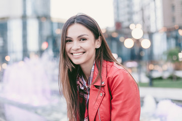 Portrait of beautiful happy cheerful brown hair young woman on evening city street with bokeh lights and fountains on background.