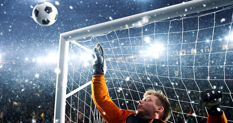 Goalkeeper tries to save from a goal on a professional soccer stadium while it's snowing.
