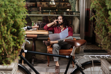 Obraz premium Distance connection. Handsome long haired man making a call while holding the menu in the restaurant