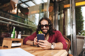 Modern smartphone. Cheerful positive man smiling while using his mobile gadget