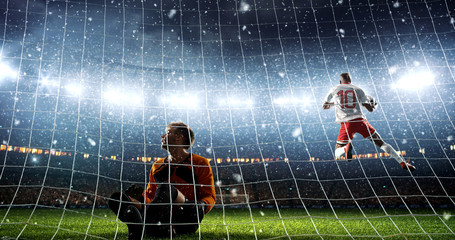 Attacker scores a goal and celebrates victory on a professional soccer stadium while it`s snowing.
