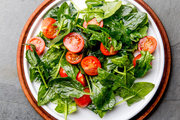 Fresh summer salad with baby spinach and tomatoes cherry. Top view, copy space. Slate gray background