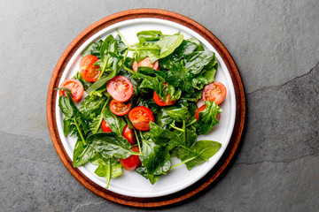 Fresh summer salad with baby spinach and tomatoes cherry. Top view, copy space. Slate gray background