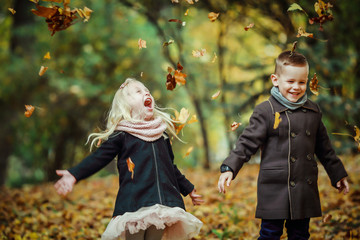 Two children, a boy and a girl throwing leaves in an autumn park. The children are having fun. 
