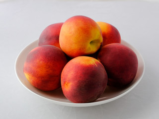 Still life of peaches. A few fresh peaches on a white plate.