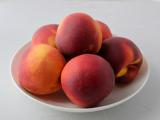 Still life of peaches. A few fresh peaches on a white plate.