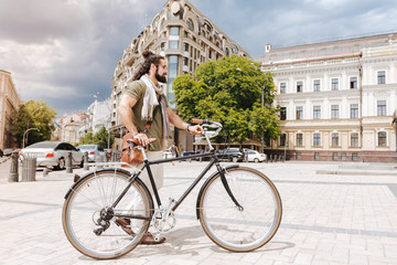 Fototapeta premium Active lifestyle. Positive nice man holing his bike while using it in the city