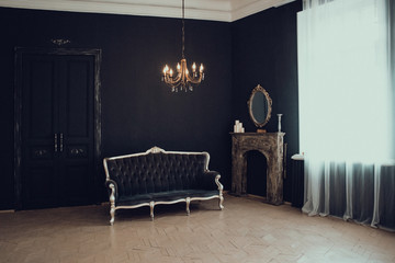 Black room in the castle with a window, a chandelier, a sofa and mirror and fireplace. Space where...