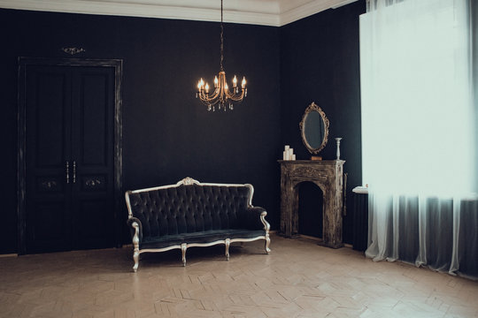 Black room in the castle with a window, a chandelier, a sofa and mirror and fireplace. Space where you can put a person.