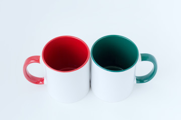 Two white mugs, with a green and red handle on a light background. 