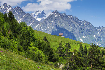 Alpine landscape of green meadow and rocky mountains in a clear sunny summer day. Amazing rural mountain scene hills in Alps with lonely house on hillside. Springtime in beautiful nature.