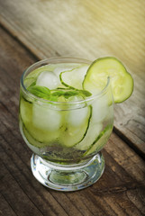 Cold fresh lemonade with cucumber, ice and mint leaves over wooden table and black background. Fresh summer drink in glass.