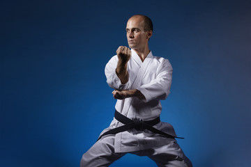 A man performs formal exercises of karate on a blue background