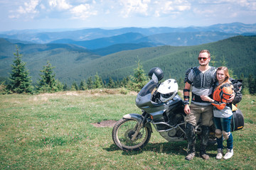 Happy young love couple in body armor and halmets stand on the top of the mountain, with big adventure motorcycle, travel togather, jorney, copy spase, mountains dirt road, enduro road trip