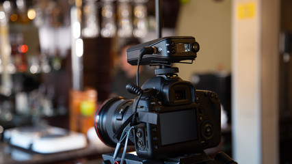 A camera on a tripod with a connected microphone records a video interview in a cafe