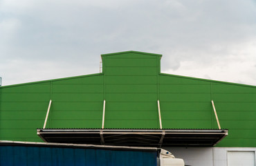 The green facade of a huge warehouse with stairs leading to the roof against a stormy sky