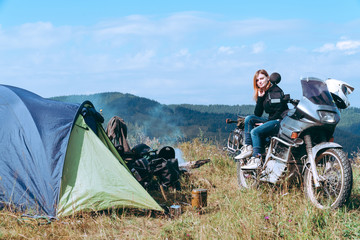 Fototapeta premium A girl stand alone on the top of the mountain a with big adventure touring motorcycle with bags and camping equipment, off road travel jorney, traveling together, couple, tent camp