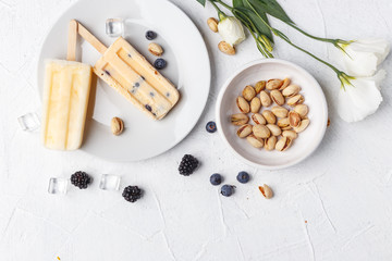 Homemade frozen ice cream popsicles from fruits and berries on table whith flowers and ingridients, top view