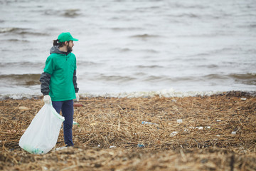 Man in green uniform cleaning shore while working on environmental conservation