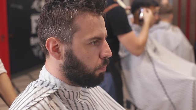 bearded man having his beard cut by hairdresser at the barbershop