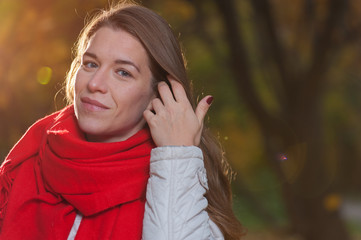 Happy autumn time. Positive beautiful woman wearing coat and red scarf on the background of nature park